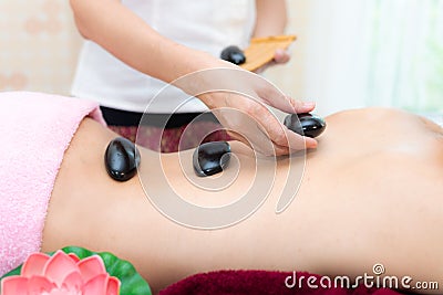 Asia beauty woman lying down on massage bed with traditional balinese hot stones along the spine at Thai spa and wellness center, Stock Photo