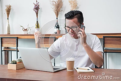 Asia casual man arm up celebrate good new from mobile at laptop Stock Photo
