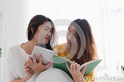Asia lesbian lgbt couple sitting on bed reading book and use tab Stock Photo
