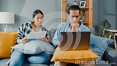 Asia young couple man and woman sit on couch serious focus on laptop computer check document paper pay bills online plan budget Stock Photo