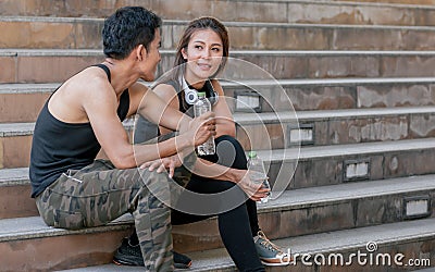 Asian adult sportive and healthy couple wearing black shirts, headphone, talking, smiling with happiness and sitting on steps Stock Photo