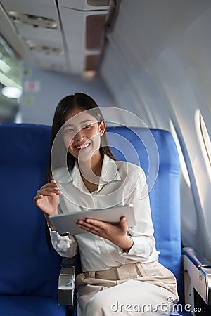 Asian attractive business woman passenger sitting on business class luxury plane while tablet computer while travel Stock Photo