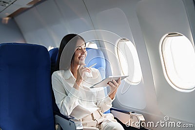 Asian attractive business woman passenger sitting on business class luxury plane while tablet computer while travel Stock Photo