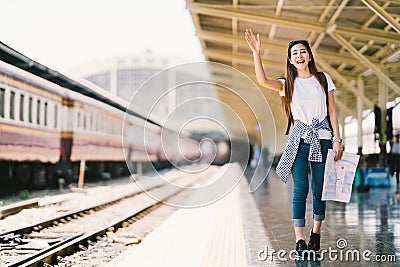 Asian backpack traveler woman holding generic local map and waving hand at train station platform summer holiday traveling concept Stock Photo