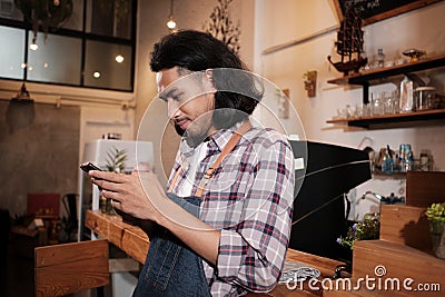 Asian barista stands at a cafe and chats about online orders on mobile phone Stock Photo