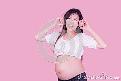 Asian beautiful pregnant woman stands relaxed and enjoys listening to music on headphones connected to the internet Stock Photo