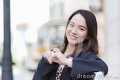 Asian beautiful woman in a dark blue long-sleeved shirt sits happy smile on a chair in an urban outdoor park Stock Photo