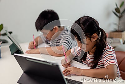 Asian boys and girls enjoy online learning by taking notes and using tablets at home Stock Photo