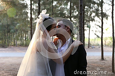 Asian bride in lovely wedding dress kisses her groom in a pine forest Stock Photo