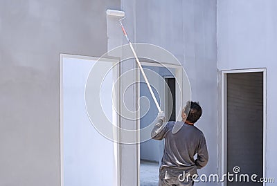 Asian builder painting primer white color on concrete wall inside of house construction site Stock Photo