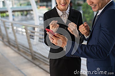 Asian businessman and businesswoman stand and looking mobile phone, cheerful and celebrated his successful in mission Stock Photo