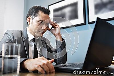 Asian Businessman in grey suit thinking and looking to his laptop. Man has stressed and headache from migraine. Stock Photo