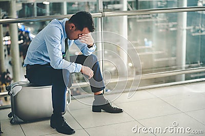 An Asian businessman is sitting on his luggage. He was stressed and looked at his smartphone at the airport Stock Photo