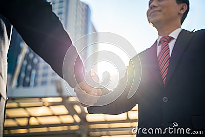 Asian businessmen making handshake in the city with highrise building in background. Partnership agreement is successful after com Stock Photo