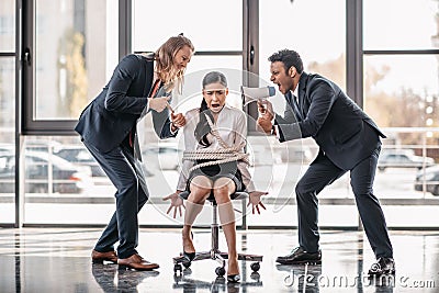 Asian businesswoman bound with rope on chair while businessmen screaming on her with megaphone Stock Photo