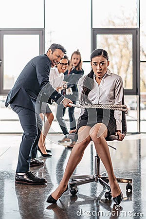 Asian businesswoman bound with rope on chair and multicultural business team pulling her Stock Photo