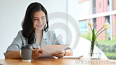 Asian businesswoman reviewing a business proposal report, analysing financial document Stock Photo