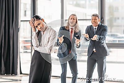 Asian businesswoman standing in office, businessmen behind gesturing and laughing Stock Photo