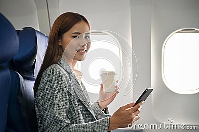Asian businesswoman using smartphone and sipping coffee during flying to somewhere by plane Stock Photo