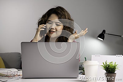 Asian businesswoman work at home with laptop and talking on smartphone and smiling. Female working on computer and using cell mobi Stock Photo