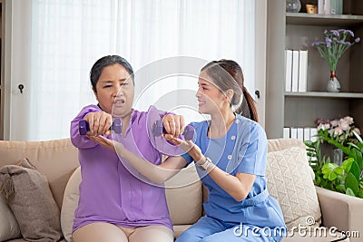 Asian caregiver woman or nurse training senior woman lifting dumbbell for arm exercise while therapy and rehabilitation. Stock Photo