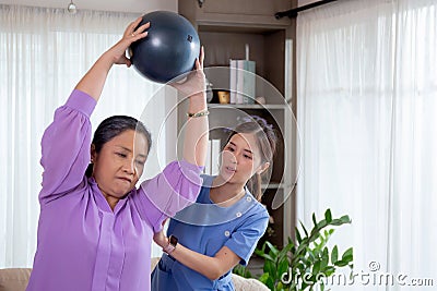 Asian caregiver woman or nurse training senior woman lifting sport ball with hands for exercise while physical therapy. Stock Photo