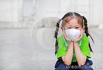 Asian child girl wearing a protection mask while outside to against PM 2.5 air pollution with pointing up in Bangkok city. Stock Photo