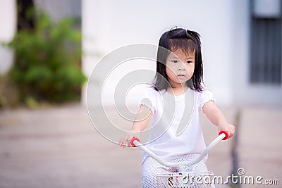 Asian child little girl is riding a bicycle on the road. Children ride a tricycle exercise bike. Stock Photo