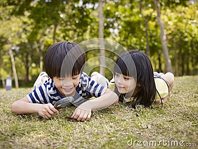 Asian children playing with magnifier outdoors Stock Photo