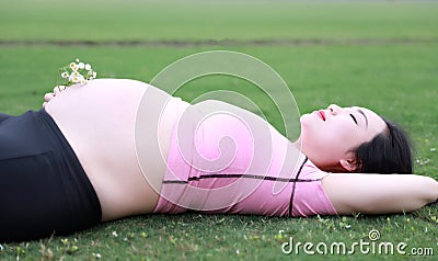 Asian Eastern Chinese happy pregnant woman lying on grass meadow in outdoor nature close eyes have a rest enjoy carefree time Stock Photo