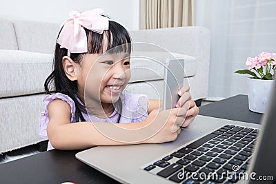 Asian Chinese little girl busy reading mobile phone and laptop Stock Photo