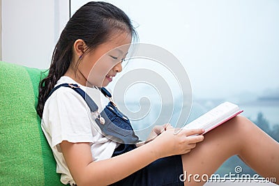 Asian Chinese little girl reading book on the windowsill Stock Photo
