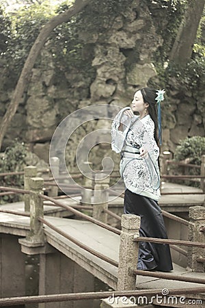 Asian Chinese woman in traditional Blue and white Hanfu dress, play in a famous garden on crooked Bridge Stock Photo