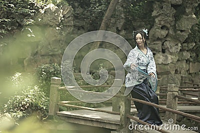Asian Chinese woman in traditional Blue and white Hanfu dress, play in a famous garden on crooked Bridge Stock Photo