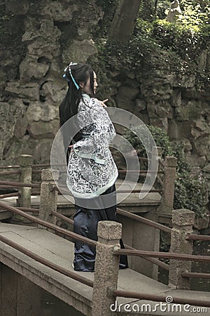 Asian Chinese woman in traditional Blue and white Hanfu dress, play in a famous garden on crooked Bridge Stock Photo