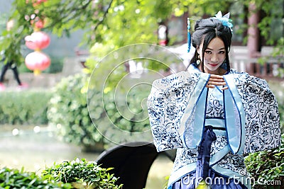 Asian Chinese woman in traditional Blue and white Hanfu dress, play in a famous garden ,sit on an ancient stone chair Stock Photo