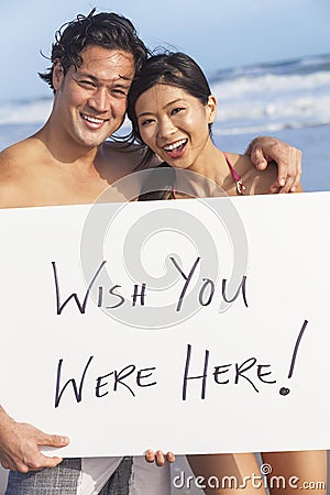 Asian Couple at Beach Wish You Were Here Sign Stock Photo