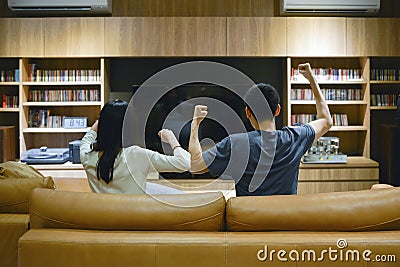 Asian couple cheering in front of TV in living room at night Stock Photo