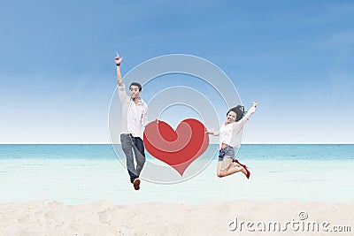 Asian couple jumping with heart card at beach Stock Photo