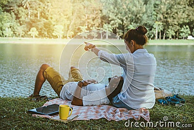 Asian couple lover sitting a relax River side in the public park. working with a notebook and drinking coffee.in the park. in the Stock Photo