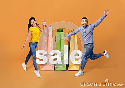 Asian Couple Near Giant Shopping Bags Jumping On Orange Background Stock Photo