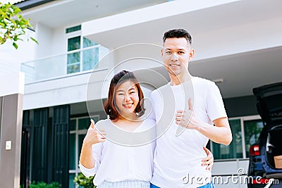 Asian couple standing in front of their new house and giving thumbs up Stock Photo
