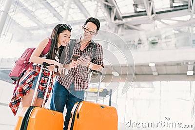 Asian couple travelers using smartphone checking flight or online check-in at airport, with passport and luggage Stock Photo