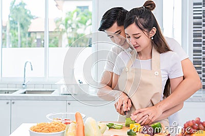 Asian couples cooking and slicing vegetable in kitchen together Stock Photo