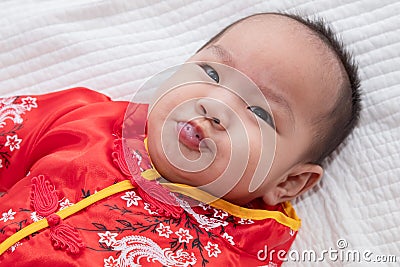 Asian cute baby boy Chinese Cheongsam costume toddler lie down on bed at home smiling laughing good humored infant Chinese Stock Photo