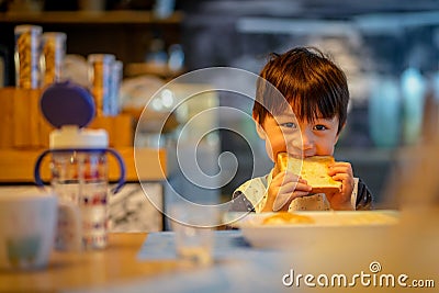 Asian cute boy show his teeth to biting big toast. Little child, caucasian boy, sitting in the dining room eating bread, for Stock Photo