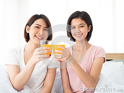 Asian cute two girls cheers glass of orange juice before drink together in the morning on white bed Stock Photo