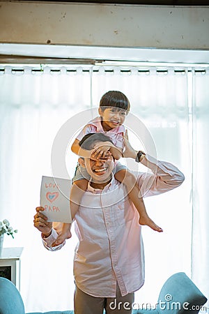 asian dad shoulders piggybacks his son showing paper love drawing Stock Photo