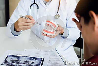 Asian dentist holding pen pointing to the dentures and is describing the problem of teeth. Stock Photo
