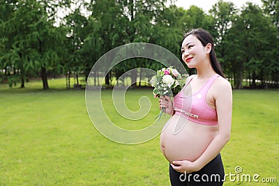 Asian Eastern Chinese young pretty pregnant girl woman mother one hand on belly one hand with bouquet expecting baby to born Stock Photo